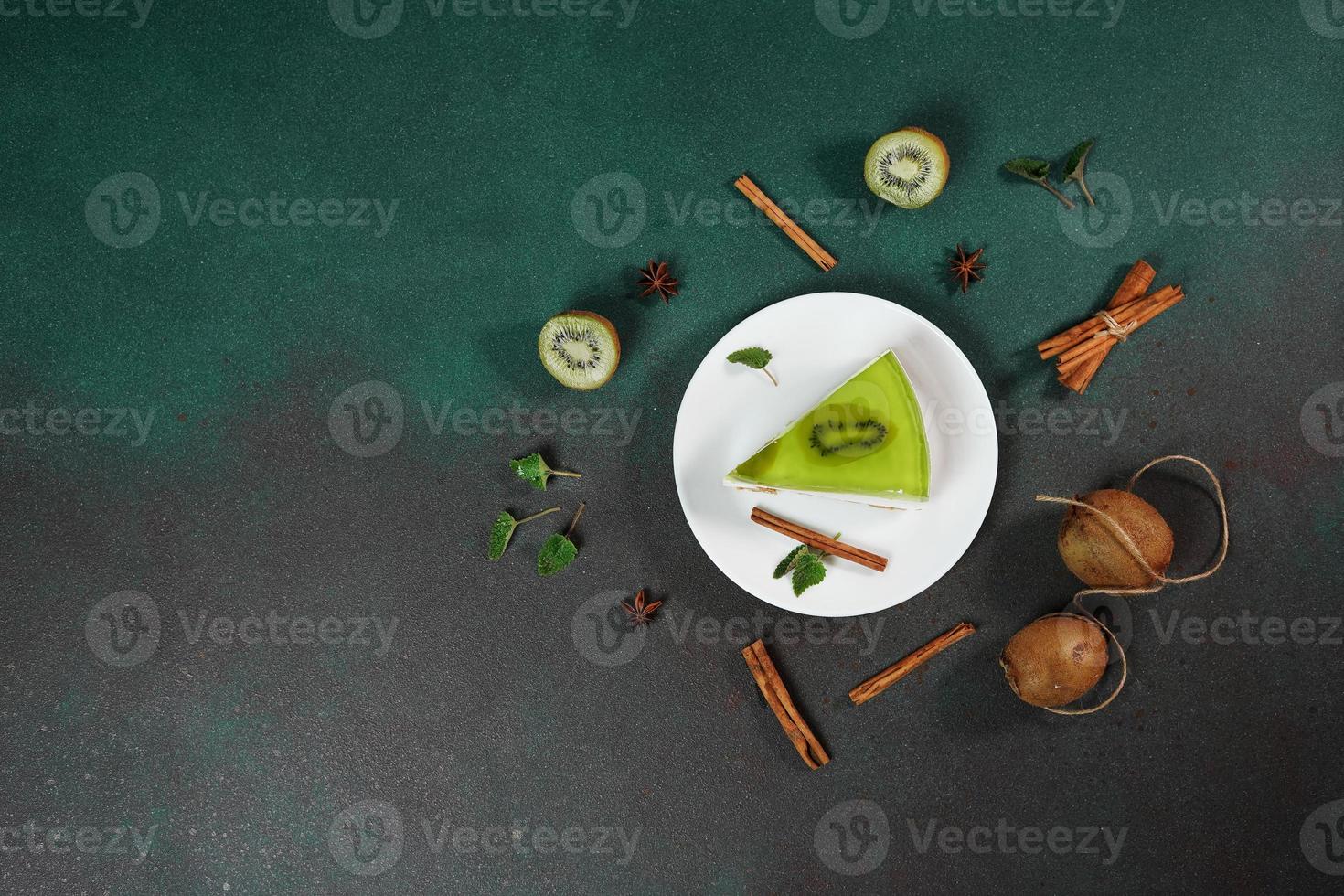 eigengemaakt kwarktaart met kiwi in een wit bord Aan een groen achtergrond. versierd met plak van kiwi, kaneel stok en bladeren munt. top visie foto