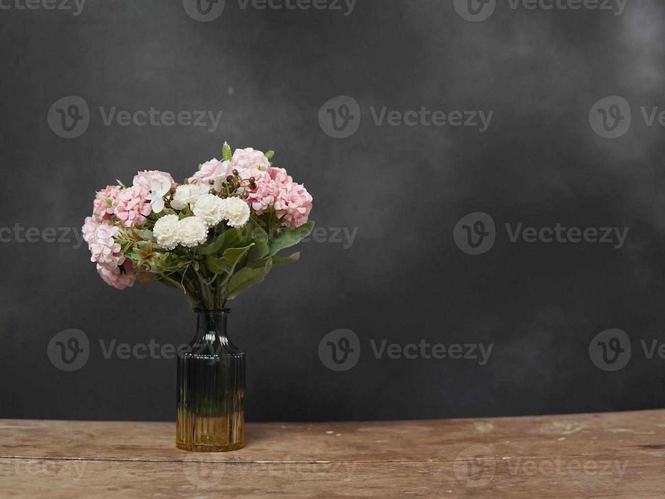 vaas met roze en wit bloemen staat Aan een houten tafel tegen een zwart wazig achtergrond. kopiëren ruimte voor tekst foto