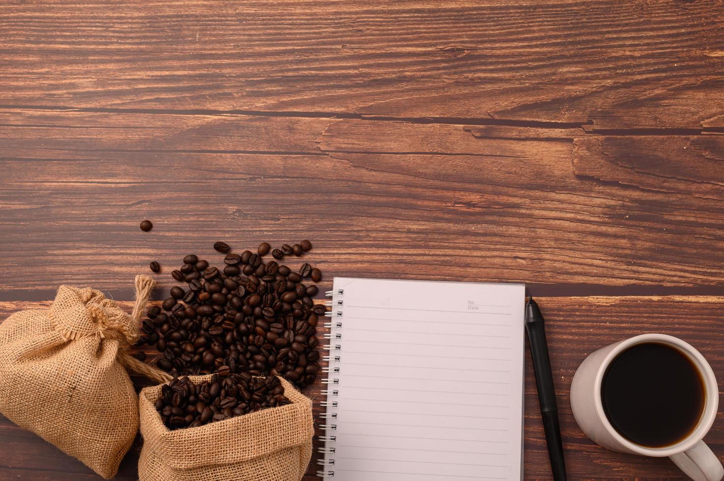 koffie, koffiebonen en een notitieboekje met een pen op een houten bureau foto