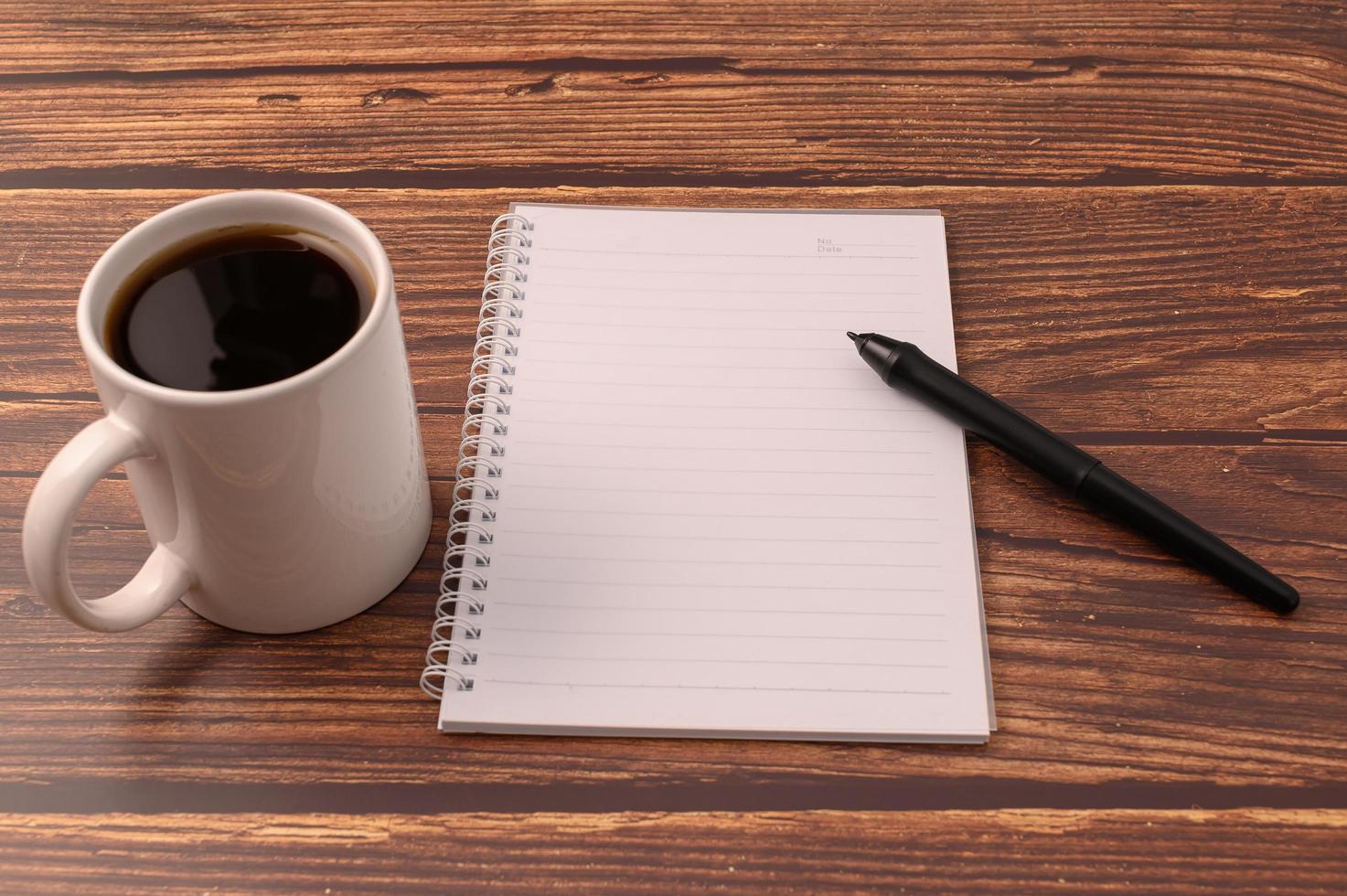 koffie en een notitieboekje met een pen op een houten bureau foto