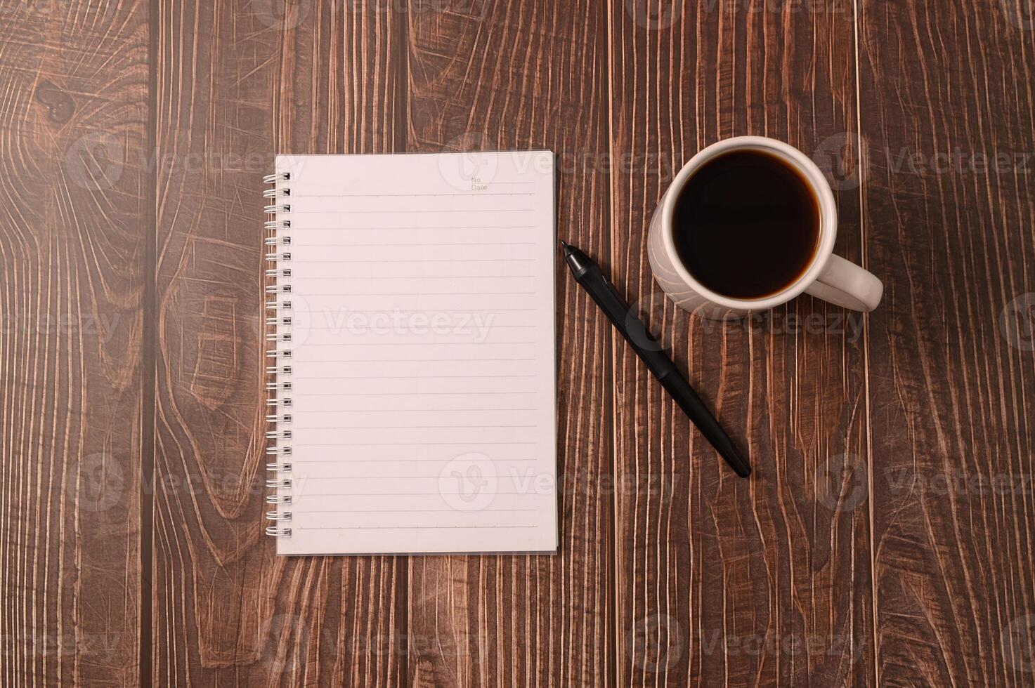 koffie en een notitieboekje met een pen op een houten bureau foto