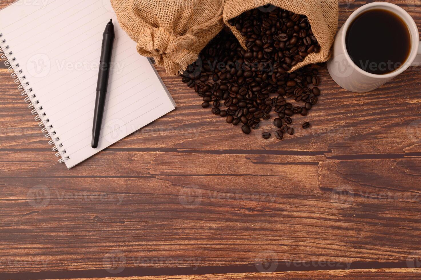 koffie, koffiebonen en een notitieboekje met een pen op een houten bureau foto