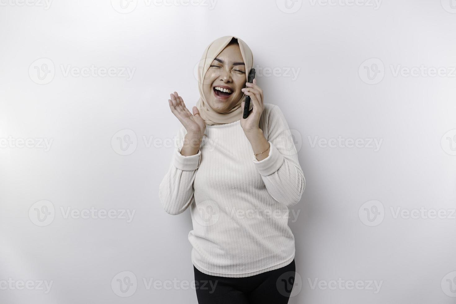 opgewonden Aziatisch vrouw vervelend hijab richten Bij de kopiëren ruimte naast haar terwijl Holding haar telefoon, geïsoleerd door wit achtergrond foto