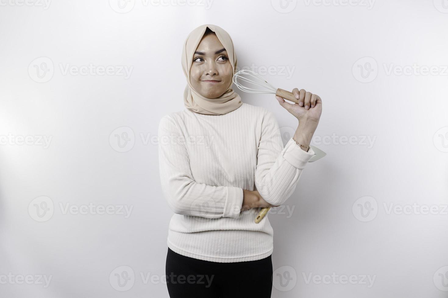 opgewonden Aziatisch moslim vrouw vervelend een hoofddoek, Holding Koken ware en lachend, geïsoleerd door wit achtergrond foto