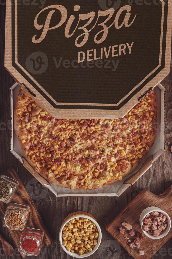 pizza met mozzarella, mais, spek en oregano in een bezorgdoos foto