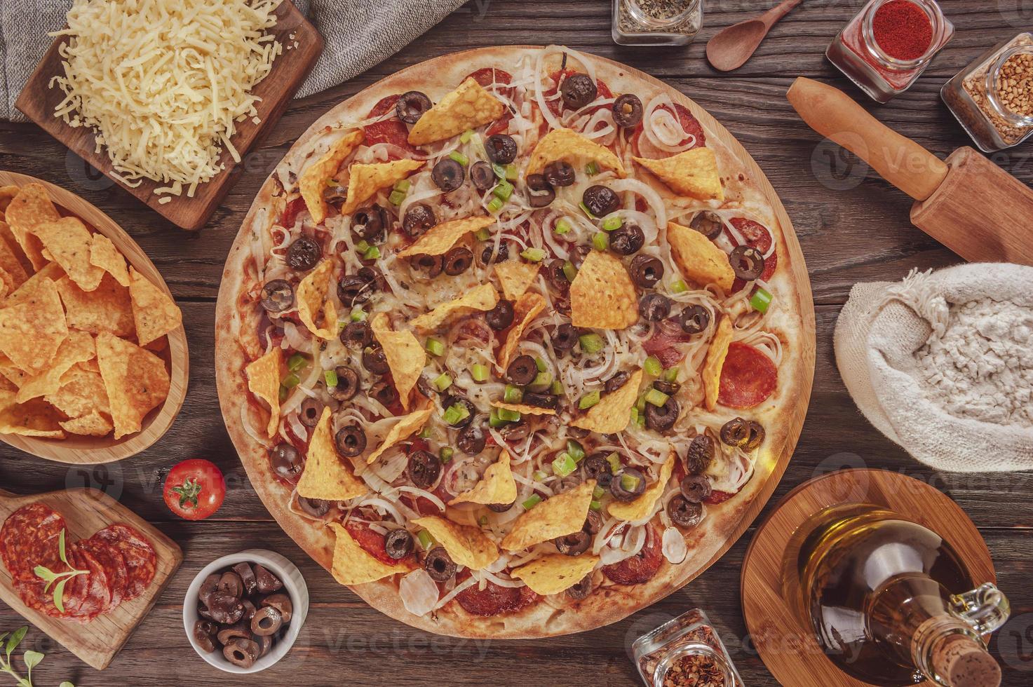 pizza met mozzarella, ui, pepperoni, zwarte olijven, groene paprika, nacho's en oregano foto