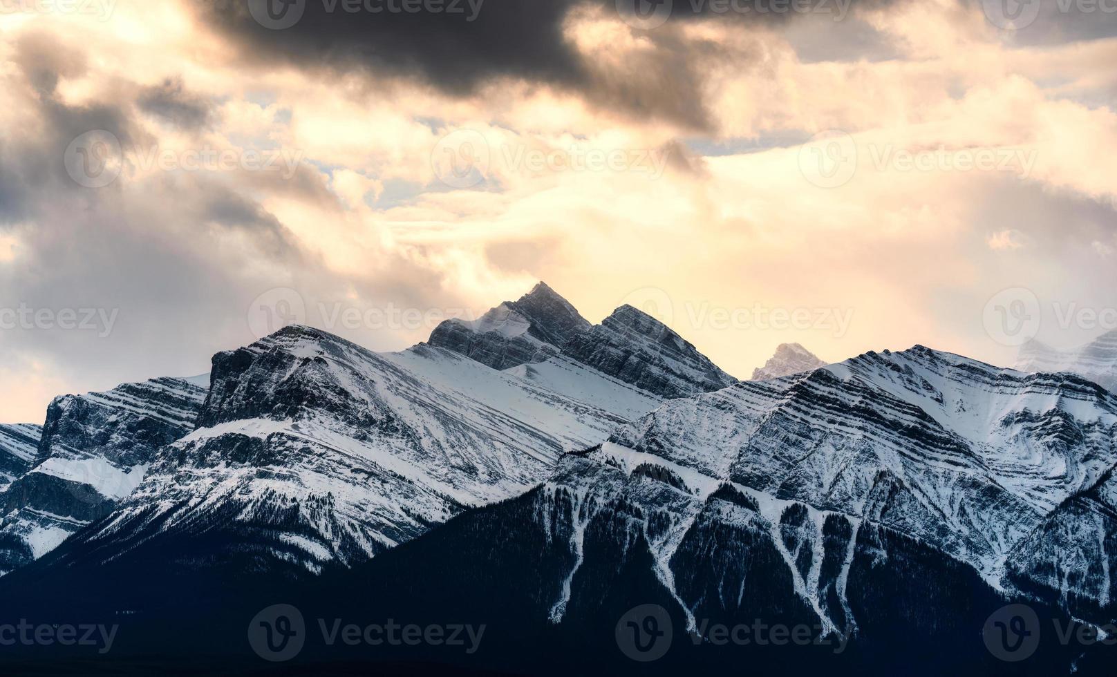 besneeuwd top rotsachtig bergen met zonlicht schijnend in wildernis Bij nationaal park foto
