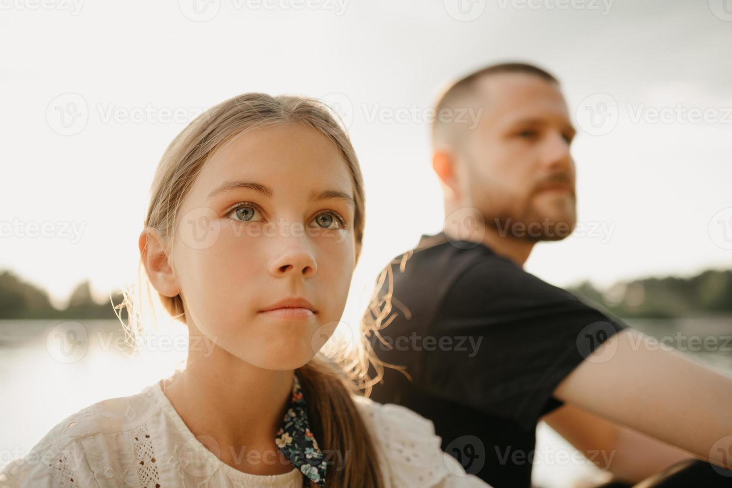 een jonge vader met baard zit met zijn dochter aan de kust van het meer foto