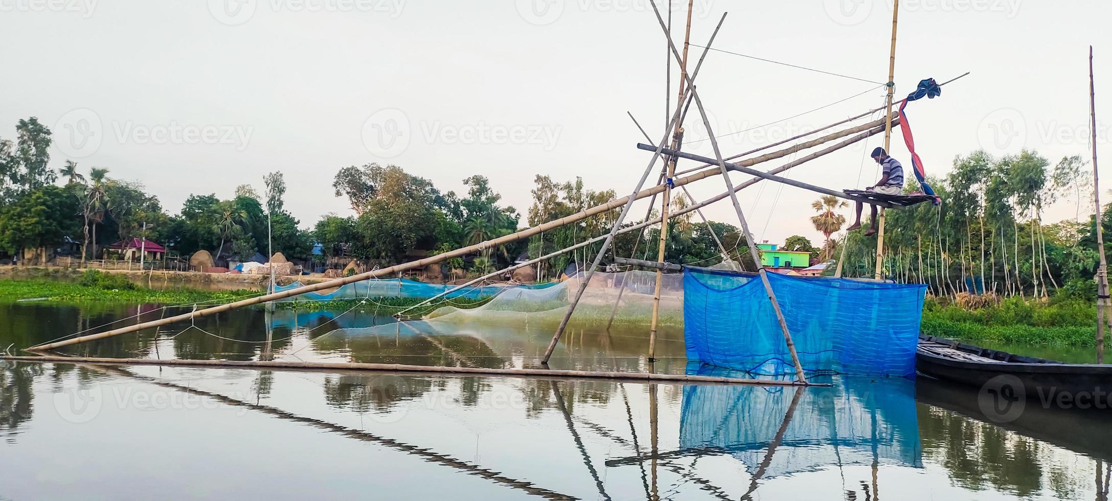 een visser visvangst met bamboe en netto val, een visser visvangst met bamboe en netto val, dorp meer boot water groen boom blauw lucht foto