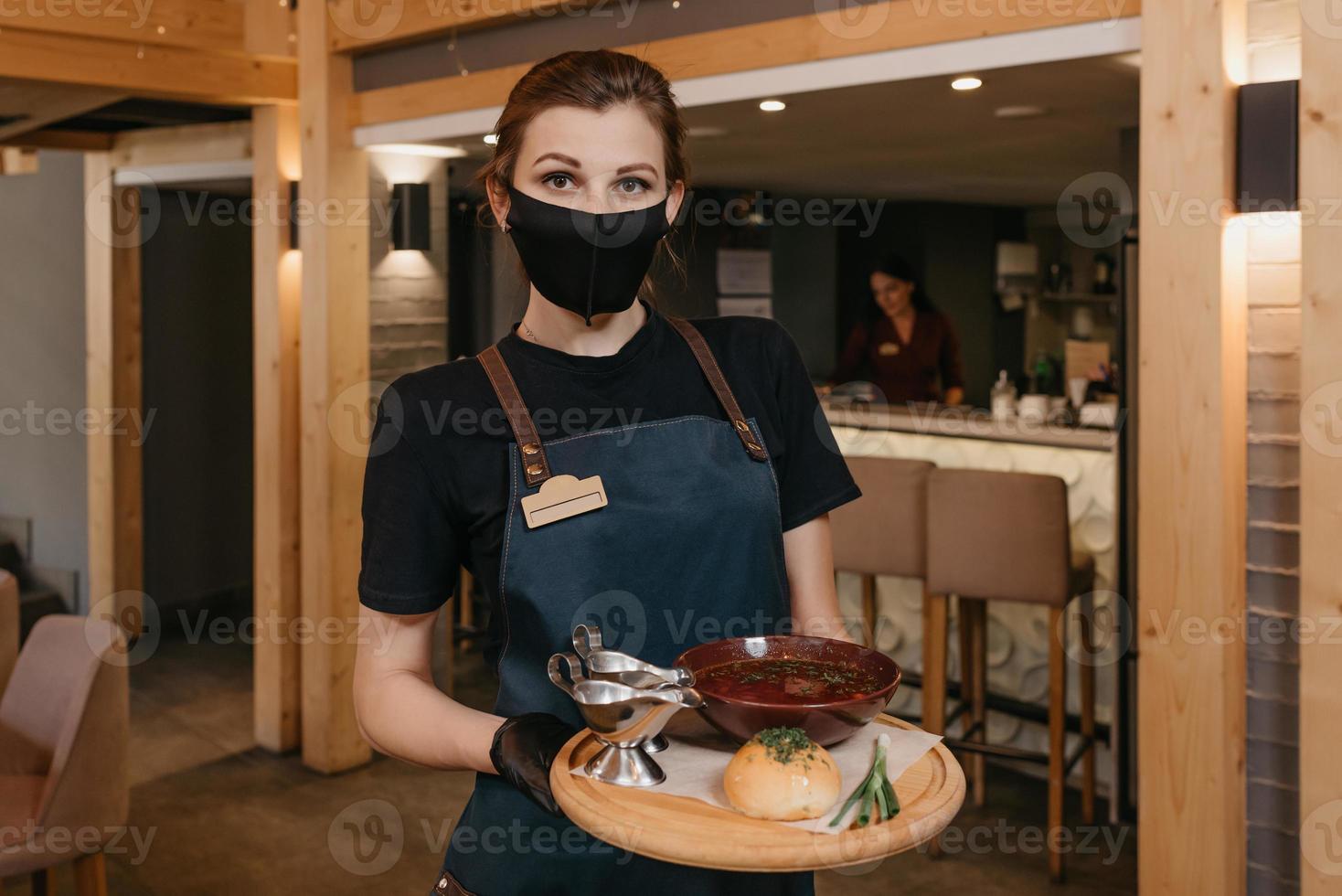een serveerster die een zwart gezichtsmasker en wegwerphandschoenen draagt, bedient klanten in een café foto