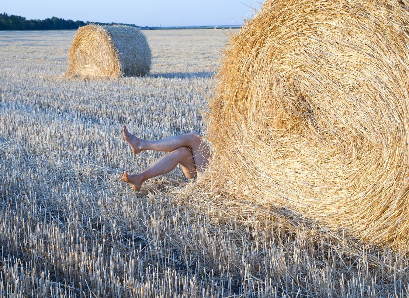 benen van een persoon die van achter een baal stro op een boerderijveld ligt foto