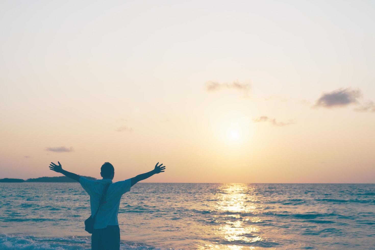 een man die zijn handen tijdens de zomervakantie opheft naar de hemel op het strand foto