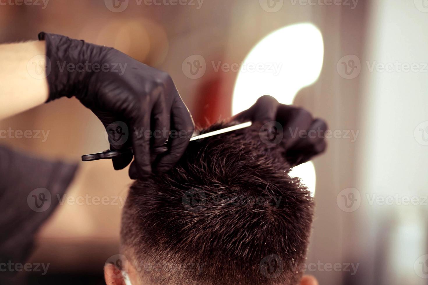 kapper met veiligheid maatregelen voor covid19, houdt schaar in zijn handen en bezuinigingen een Mens, sociaal afstand, snijdend haar- met rubber handschoenen in een schoonheid salon foto