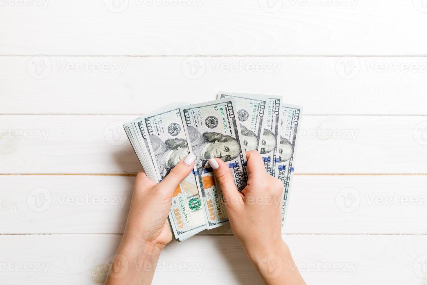 top visie van vrouw handen tellen geld. een honderd dollar bankbiljetten Aan houten achtergrond. bedrijf concept foto