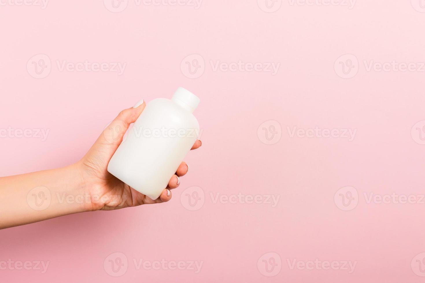 vrouw hand- Holding room fles van lotion geïsoleerd. meisje geven buis kunstmatig producten Aan roze achtergrond foto