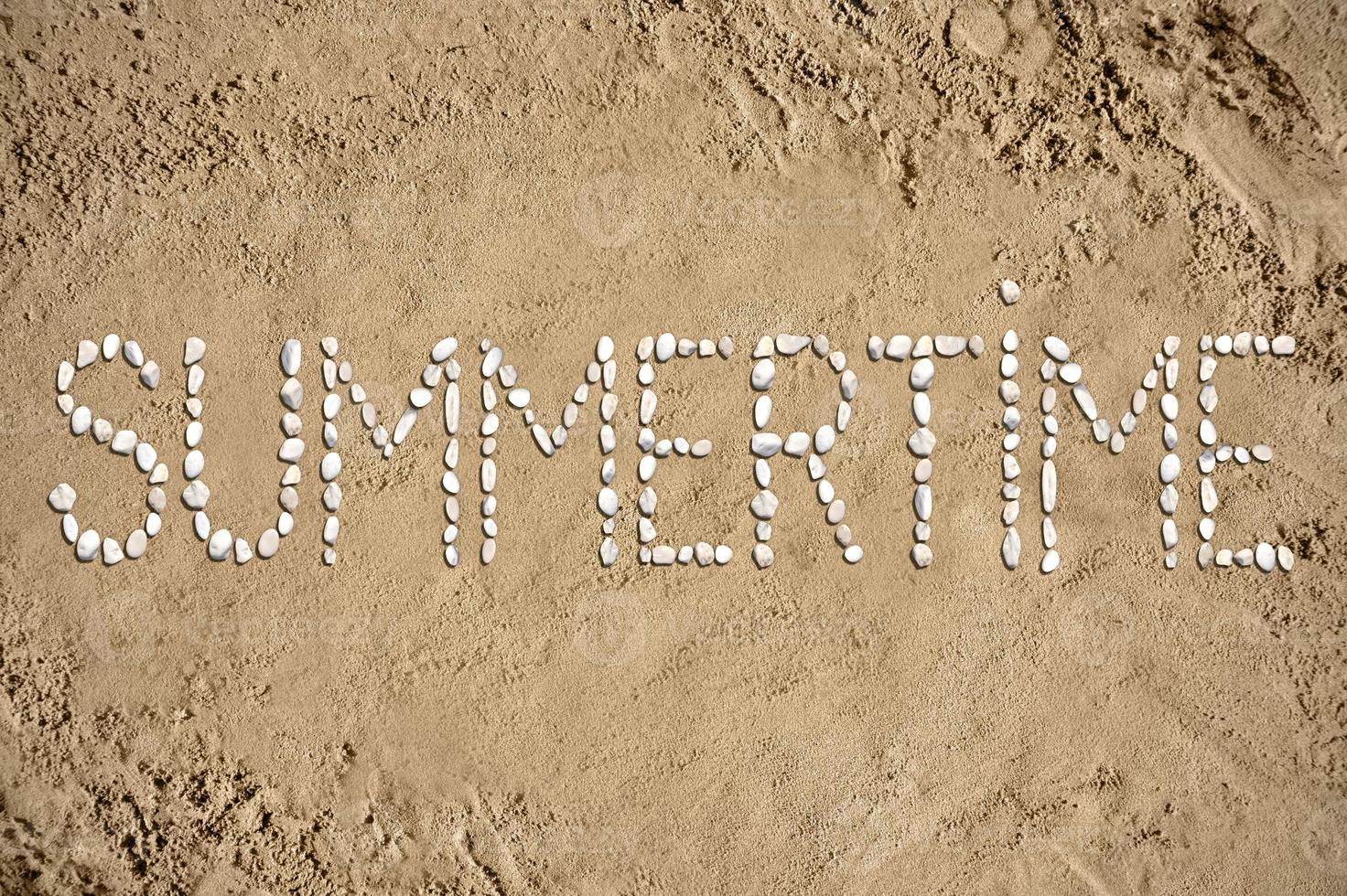 zomertijd - woord gemaakt met stenen Aan zand foto