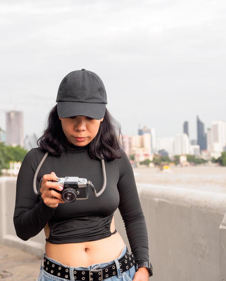 portret toerist jong vrouw Aziatisch vervelend zwart hoed en zwart jurk met retro film camera naar nemen afbeeldingen. opslaan herinneringen van uw reist foto