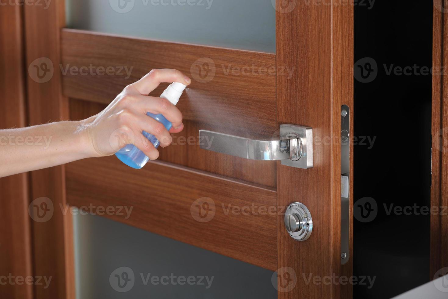persoon die desinfectiemiddel op een deurkruk sproeit foto