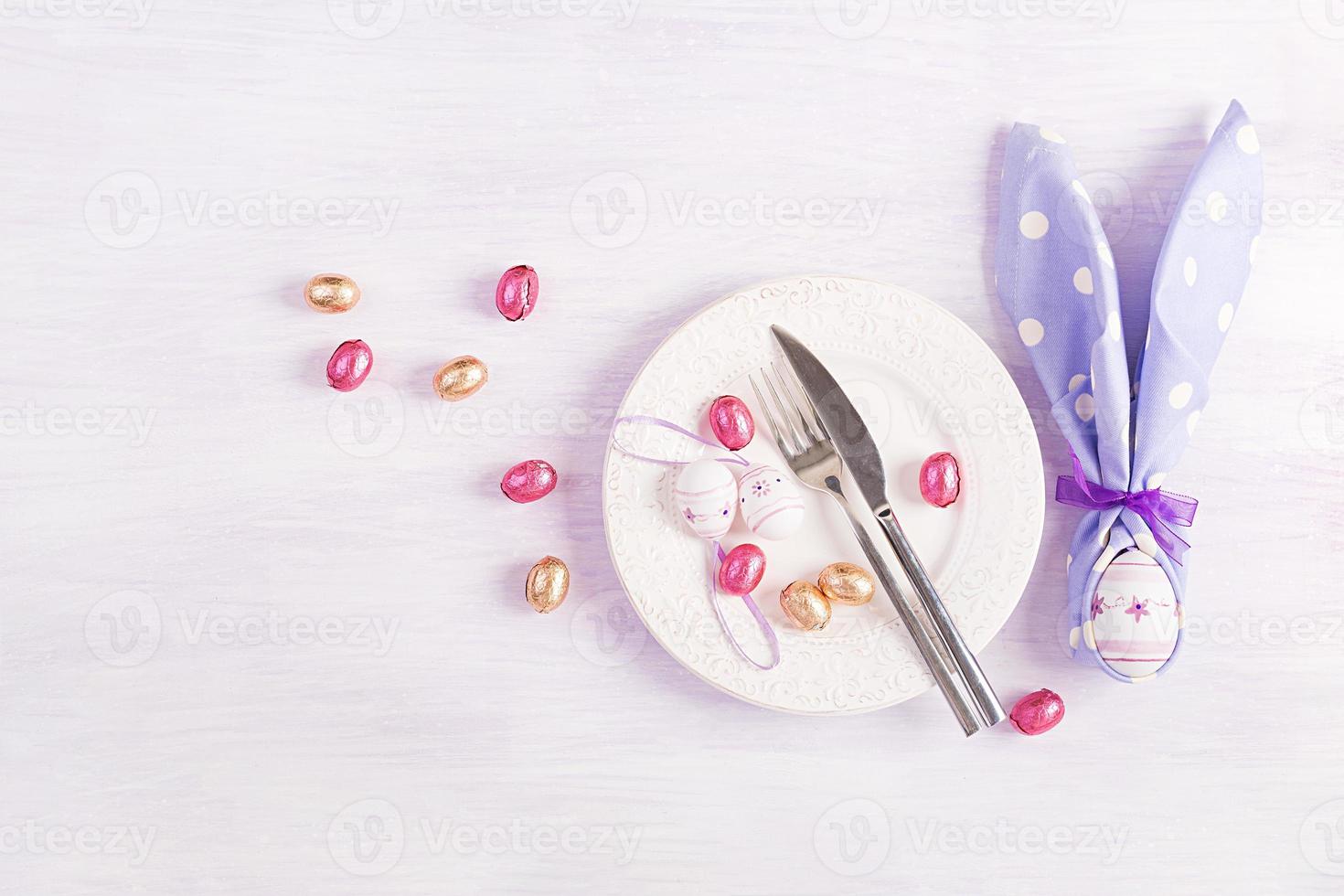Pasen tafel instelling. wit bord met een servet gevouwen in de vorm van een konijn, Pasen en chocola eieren Aan een roze achtergrond. gelukkig Pasen vakantie concept. top visie, vlak leggen foto