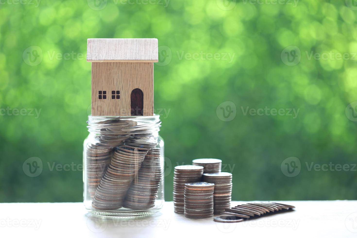 model huis op munten in glazen fles op natuur groene achtergrond foto