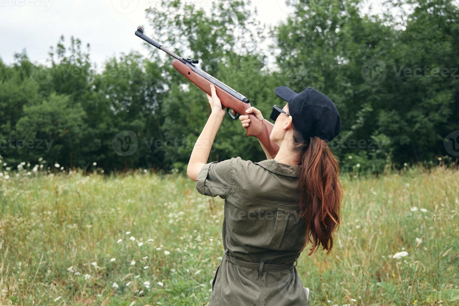 vrouw Aan buitenshuis Holding een geweer omhoog groen jumpsuit jacht- levensstijl zwart pet foto