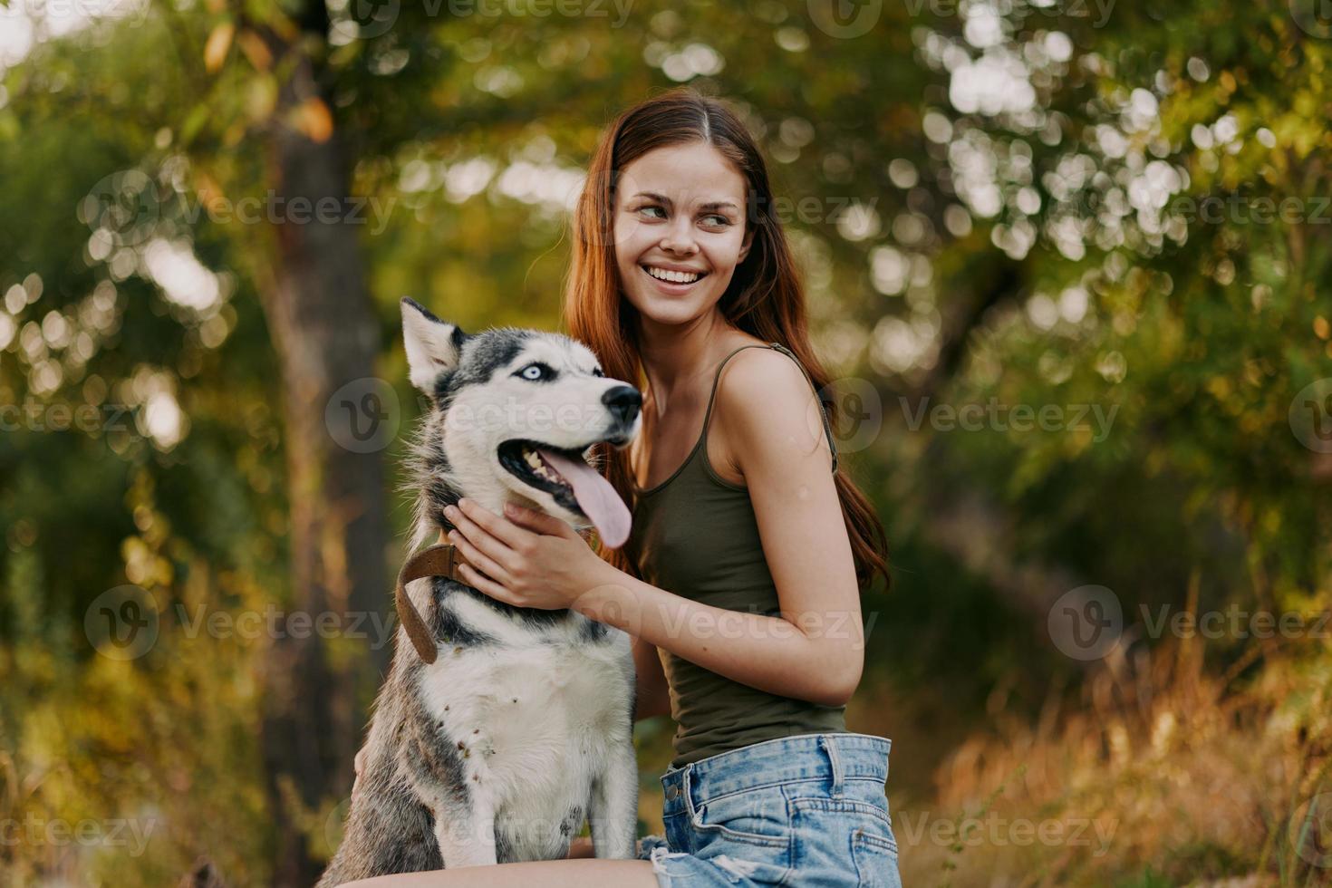 een vrouw met een schor ras hond glimlacht en liefdevol beroertes haar geliefde hond terwijl wandelen in natuur in de park in herfst tegen de backdrop van zonsondergang foto