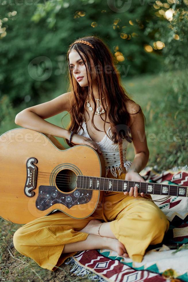 een meisje in eco-kleding hippie zittend met een gitaar en op zoek Bij een zonsondergang in de zomer foto