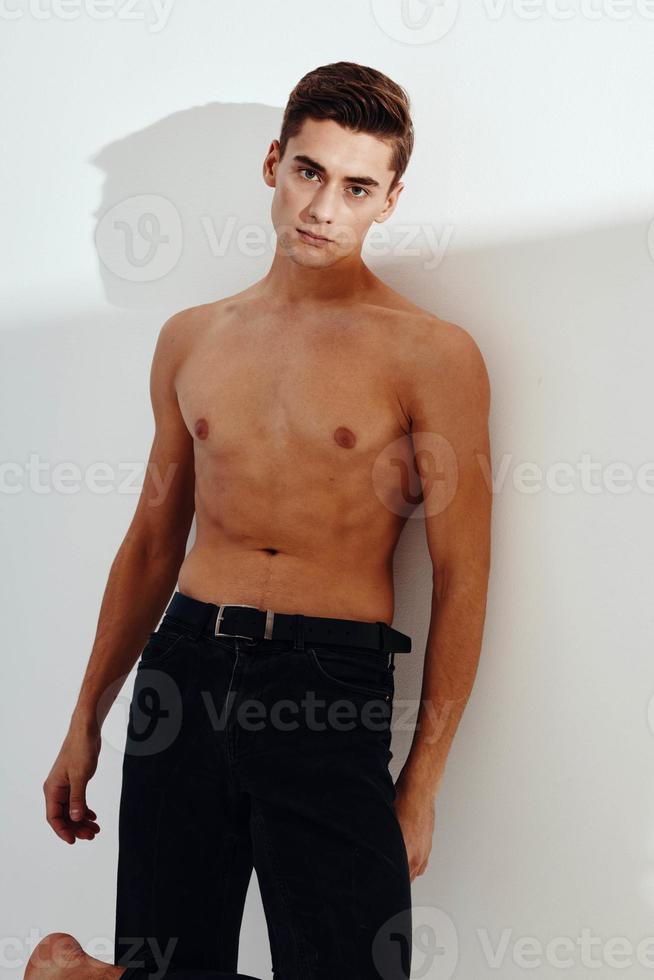 een knap Mens met een naakt torso en in zwart broek gebaren met zijn handen Aan een licht achtergrond foto