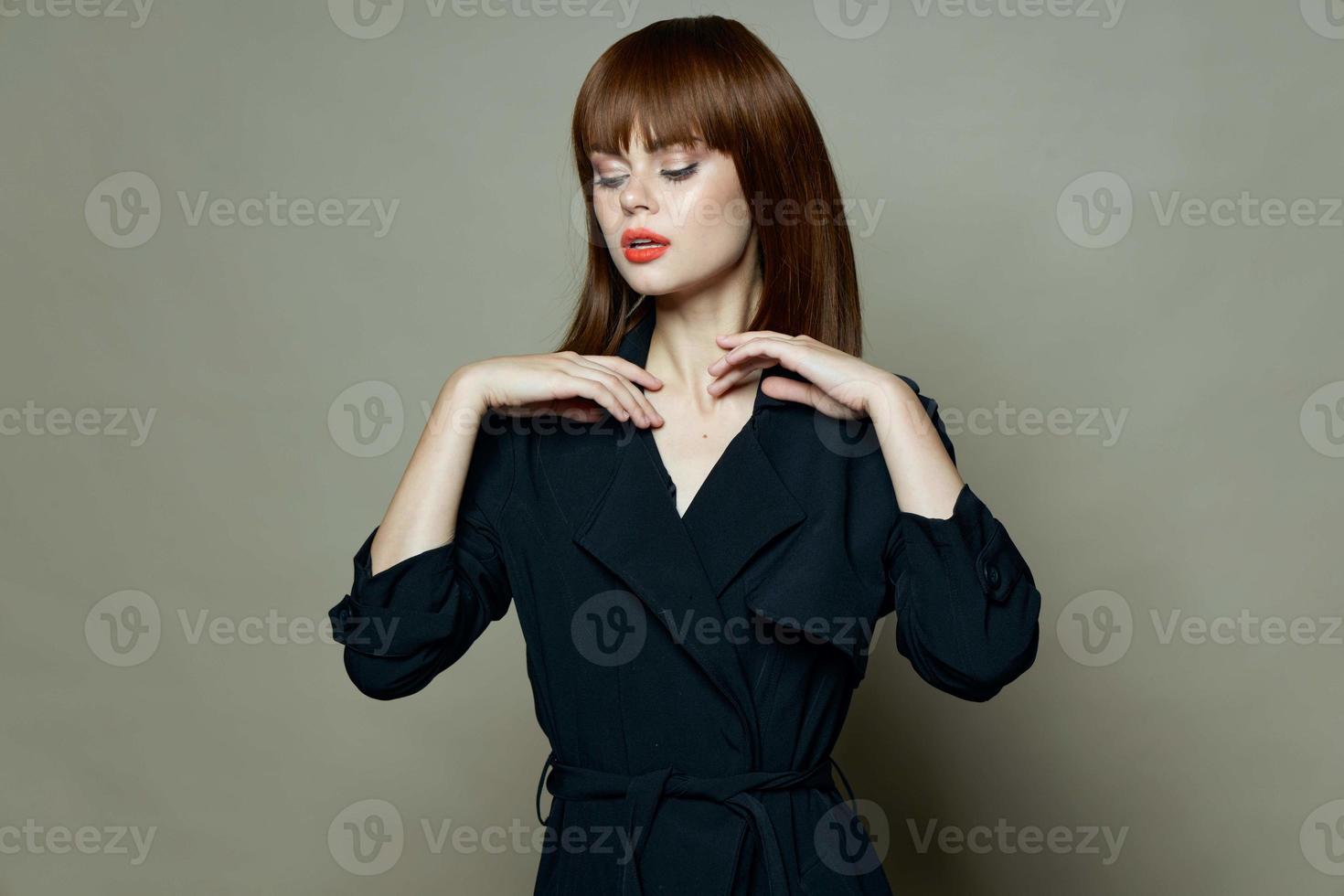 vrouw met rood lippen in een zwart jas houdt handen in de buurt de gezicht. foto