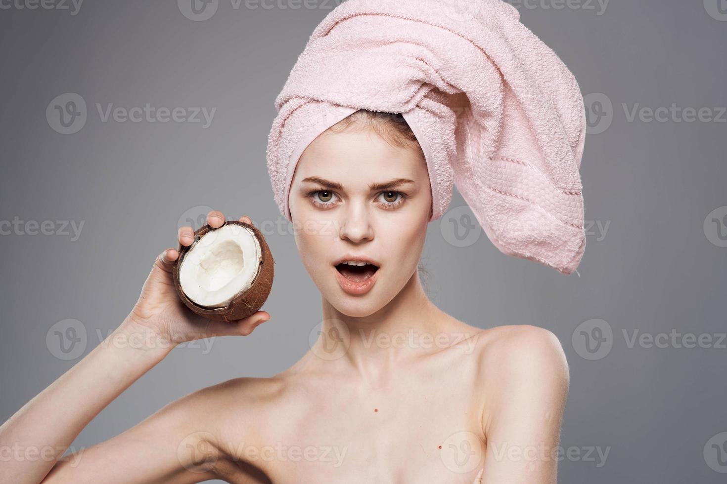 vrouw met naakt schouders met een kokosnoot in haar handen schoon huid exotisch natuurlijk schoonheidsmiddelen grijs achtergrond foto