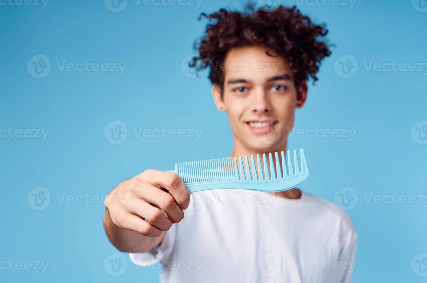 gelukkig vent met een kam in zijn hand- Aan een blauw achtergrond en gekruld haar- brunette model- foto