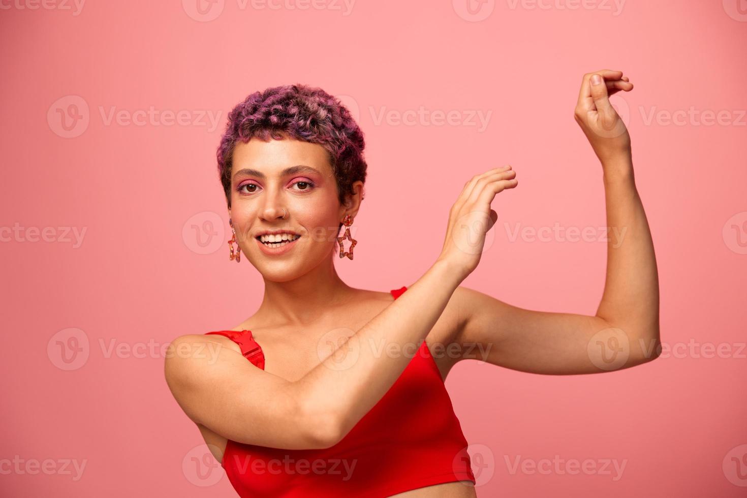 mode portret van een vrouw met een kort kapsel van Purper kleur en een glimlach met tanden in een rood top Aan een roze achtergrond geluk foto