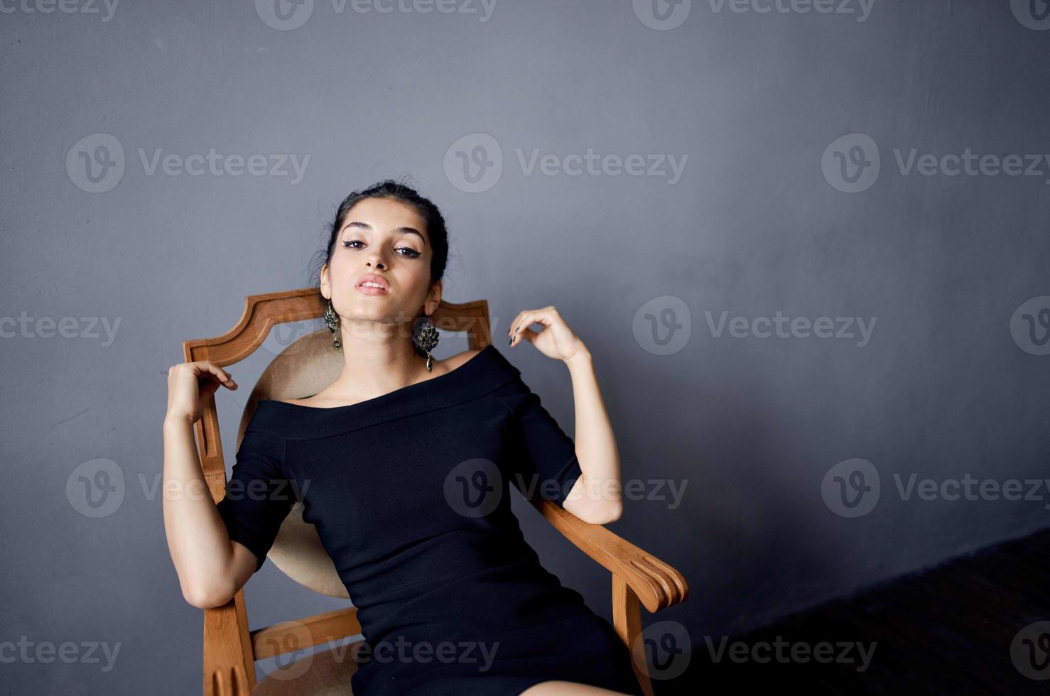 brunette oorbellen sieraden poseren in de buurt de stoel zwart jurk geïsoleerd achtergrond foto