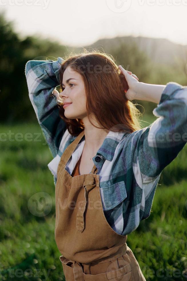 portret van een jong meisje Aan een zomer dag in de stralen van de instelling zon met een mooi glimlach, gekleed net zo een boer en tuinman foto