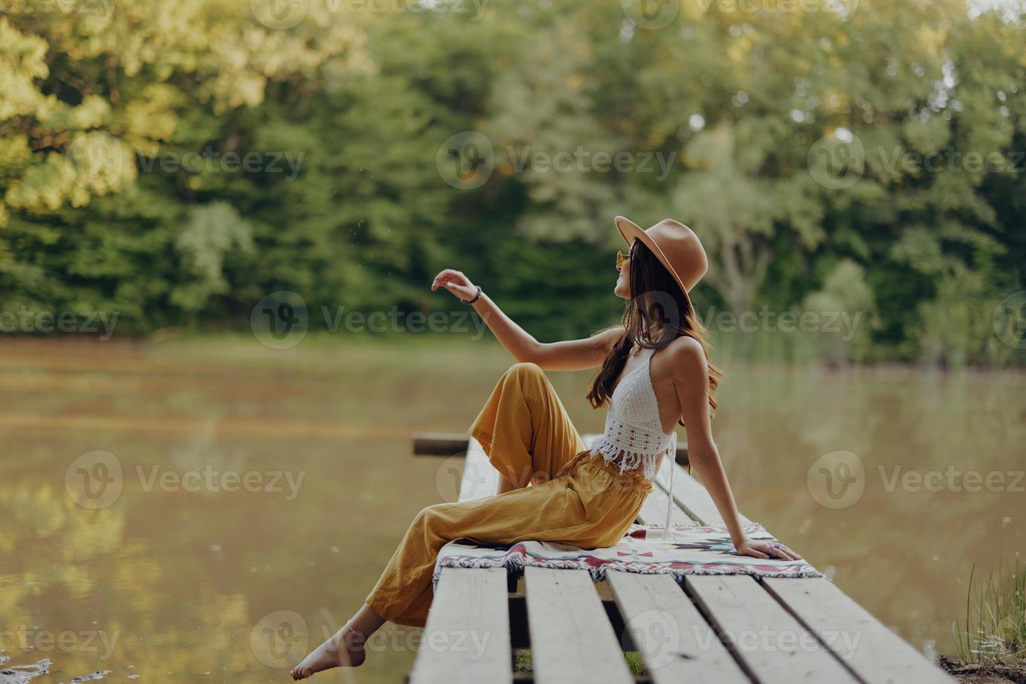 een hippie vrouw zit Aan een brug door de rivier- en geniet de mooi landschap in de omgeving van haar, gelukkig in de zonsondergang van de herfst zon foto