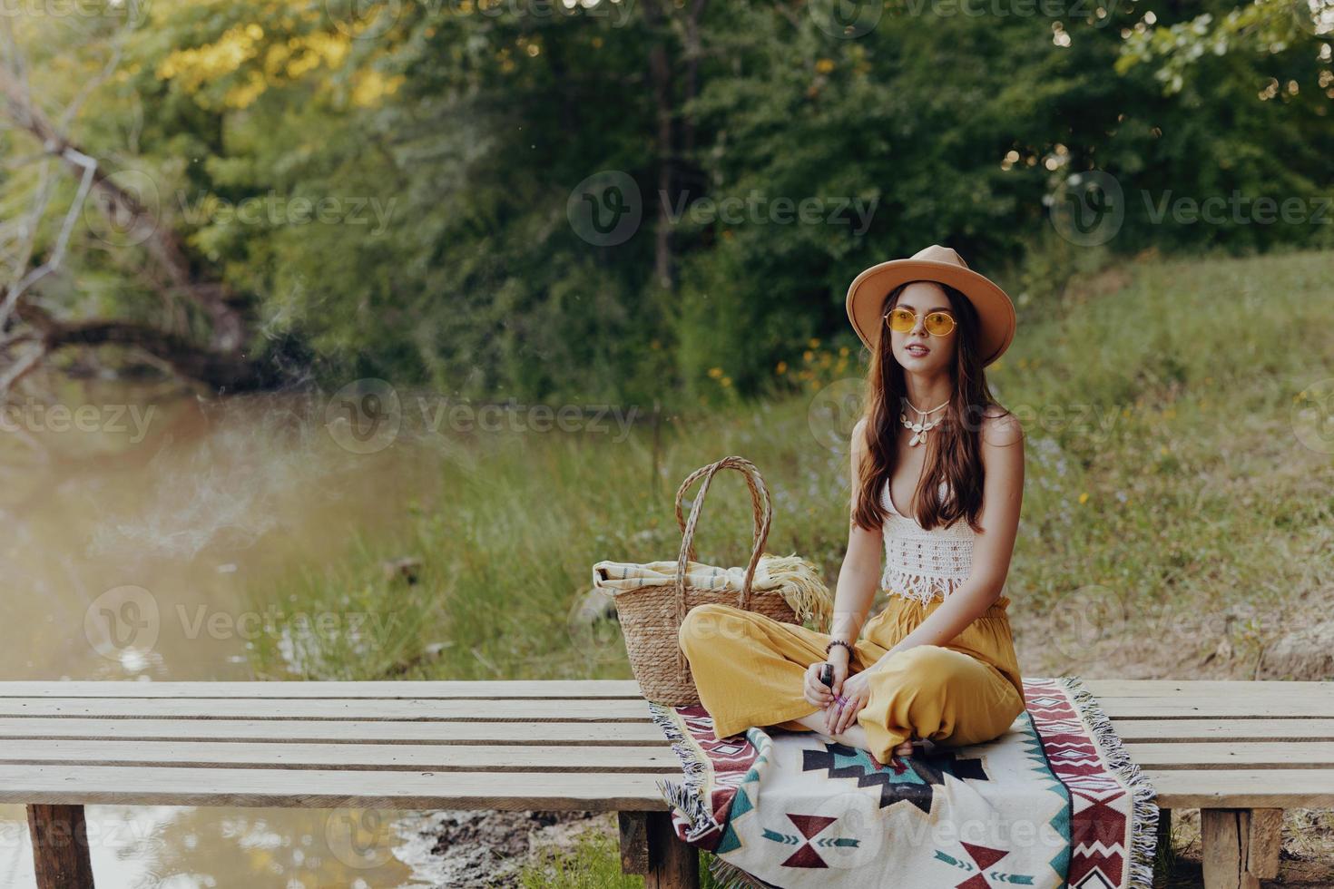 vrouw in hippie kleren zittend in natuur door de meer Aan een brug ontspannende en bewonderend de landschap foto