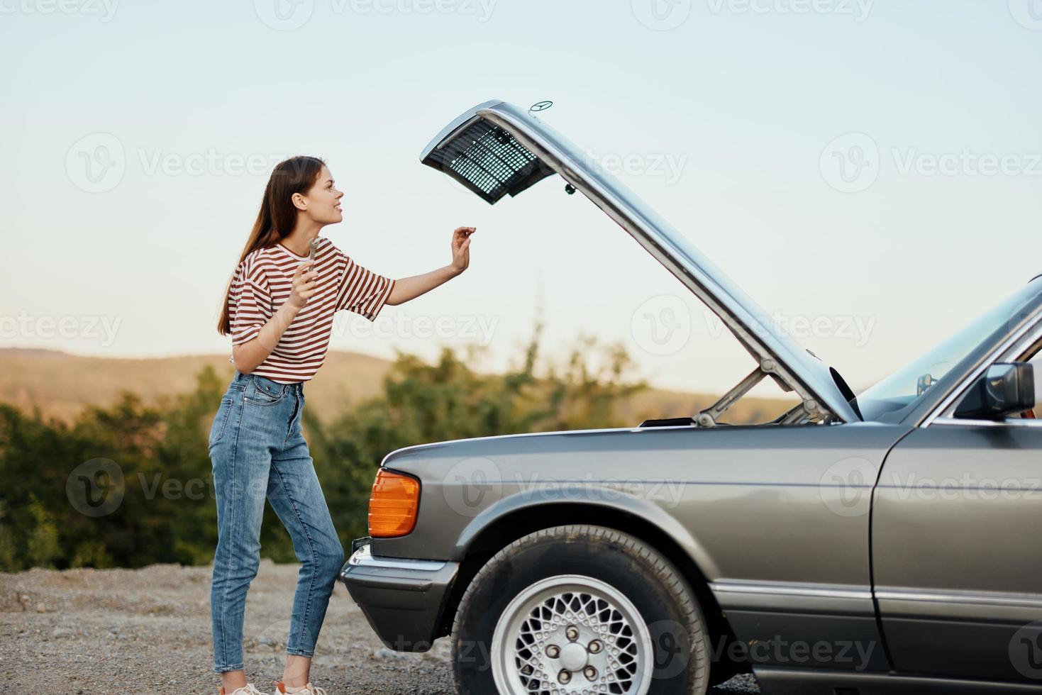 een vrouw staat buiten een kapot, gevaarlijk oud auto met een moersleutel Aan de weg op reis alleen foto