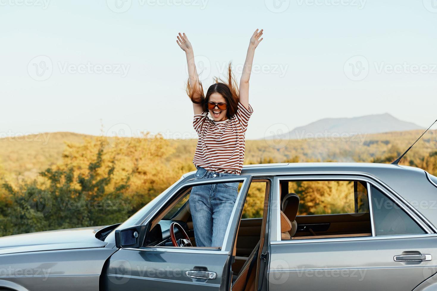 gelukkig vrouw reiziger beklommen Aan de auto en verspreiding haar armen glimlachen gelukkig. looks Bij de natuur in de omgeving van. levensstijl in reizen en vreugde foto