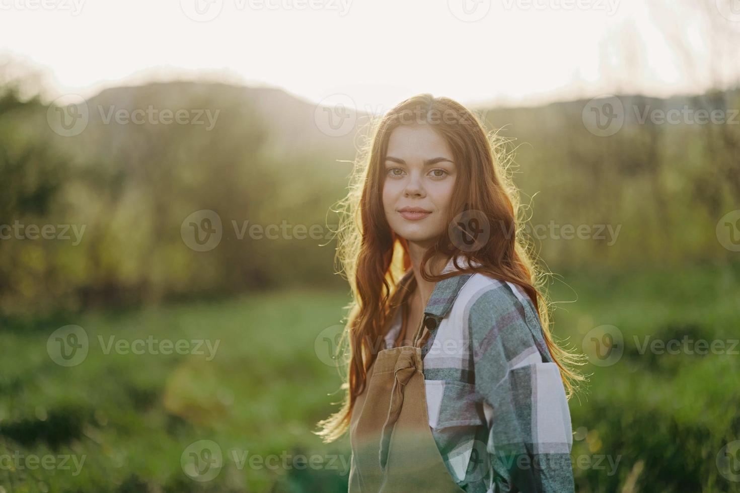 portret van een jong glimlachen vrouw in werk kleren geruit overhemd en schort in natuur in de avond na werk foto