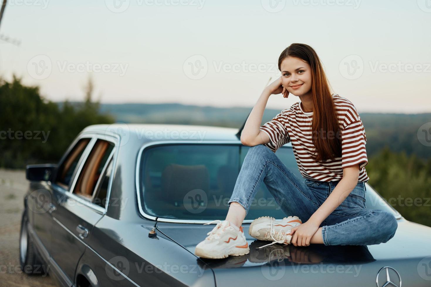 een jong vrouw reist alleen in haar auto Aan de wegen in de platteland en ontspant zittend Aan de kap aan het kijken de zonsondergang foto