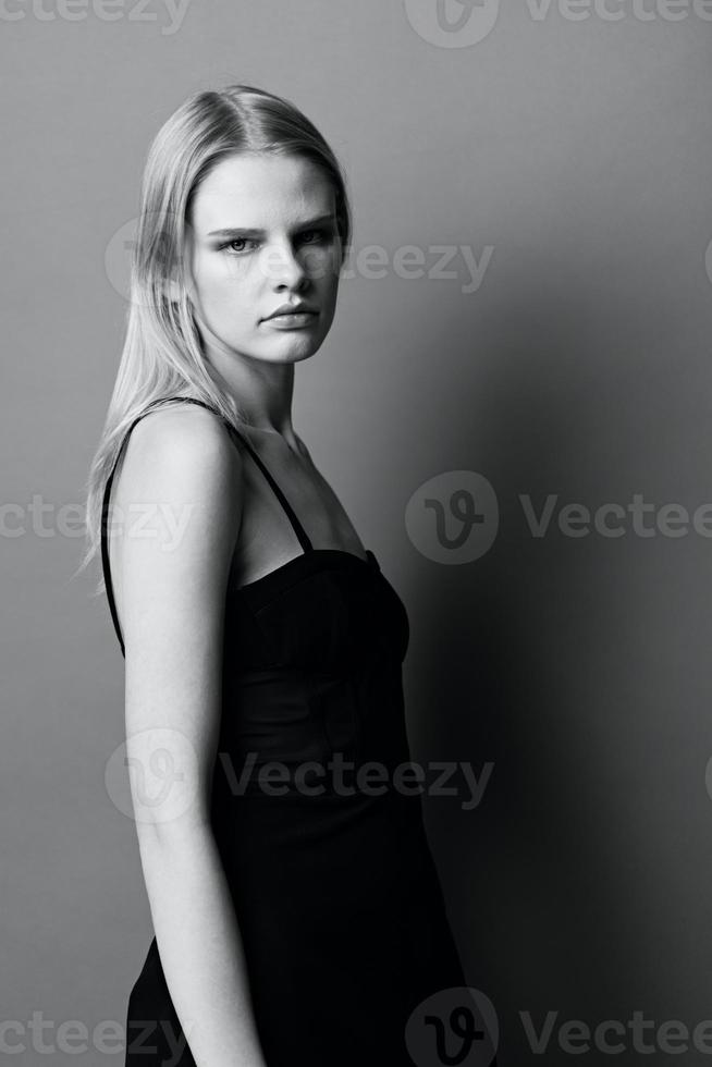 elegant zwart en wit portret in studio met prachtig professioneel blond jong vrouw vrouw in weinig zwart jurk looks Bij camera poseren geïsoleerd. koel aanbod voor mode merken foto