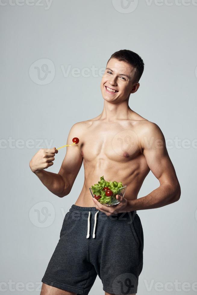 vrolijk vent met gemotiveerd omhoog gespierd buikspieren bord salade eetpatroon voedsel geïsoleerd achtergrond foto