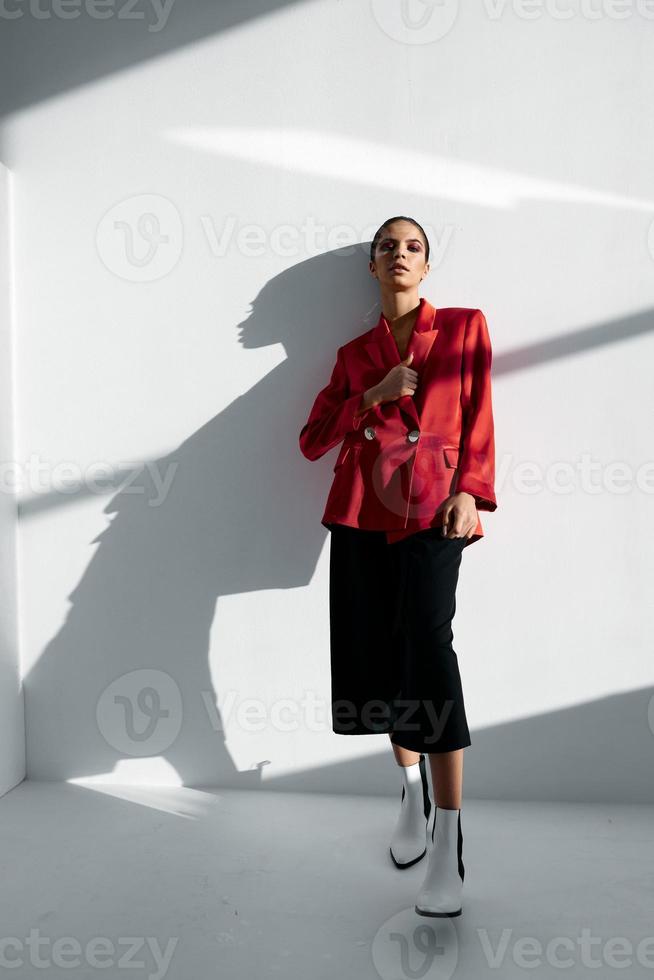 een vrouw in een rood jasje en modieus broek leunde tegen de muur foto