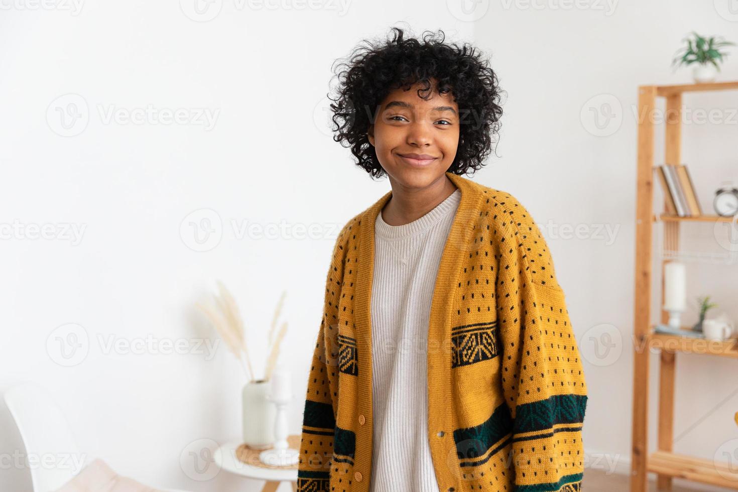 mooi Afrikaanse Amerikaans meisje met afro kapsel glimlachen Bij huis binnen. jong Afrikaanse vrouw met gekruld haar- lachend in leven kamer. vrijheid geluk zorgeloos gelukkig mensen concept. foto