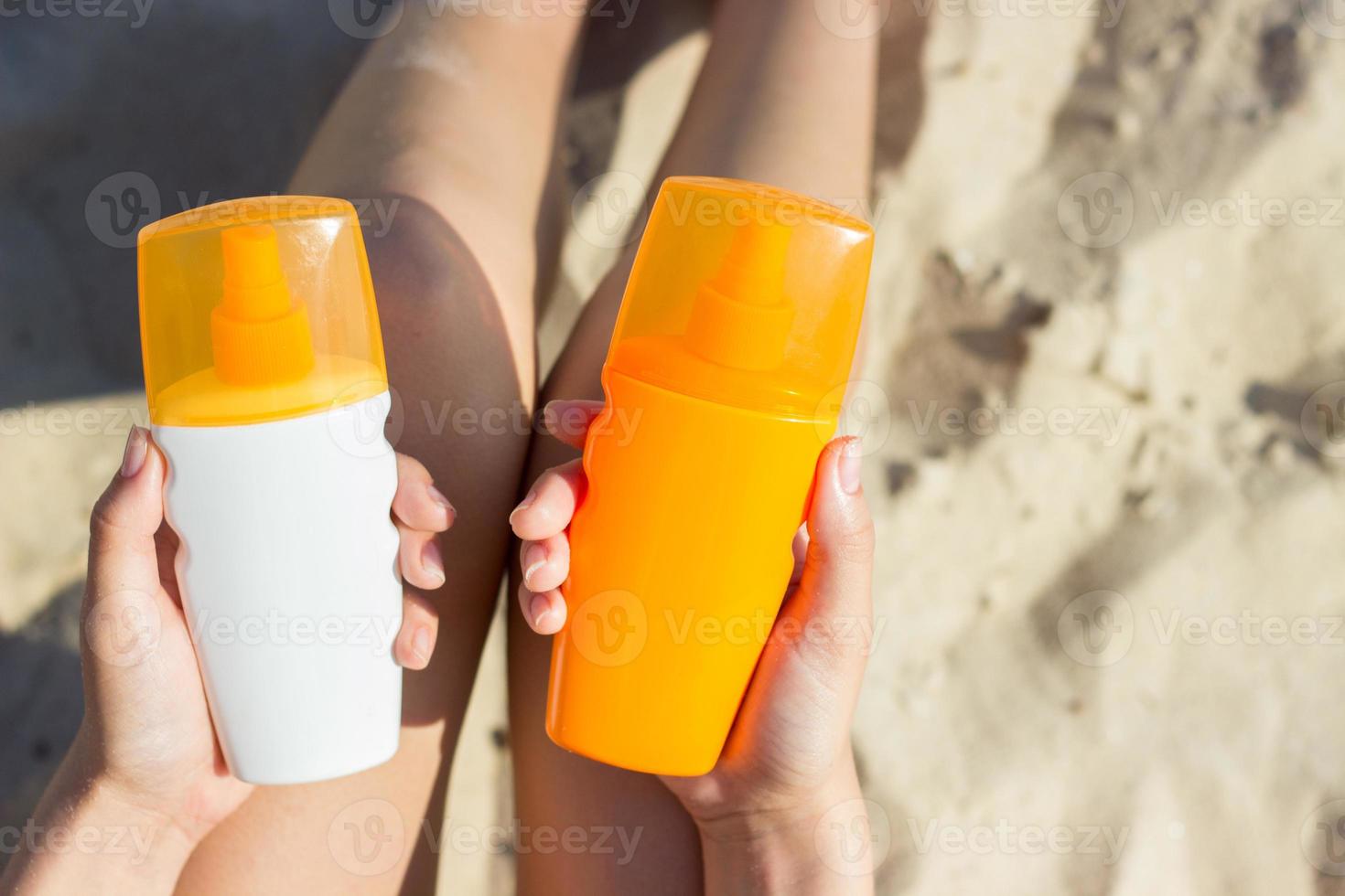 een vrouw Holding twee flessen van zonnescherm in haar handen. een meisje kiest tussen twee flessen van zonnescherm foto