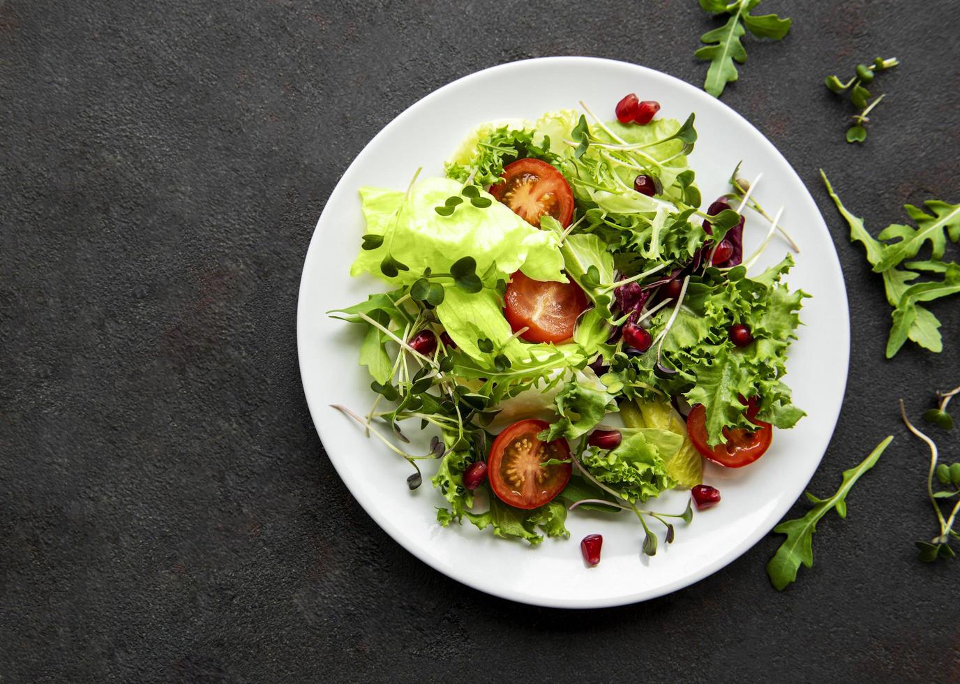 verse groene gemengde slakom met tomaten en microgreens op zwarte concrete achtergrond foto