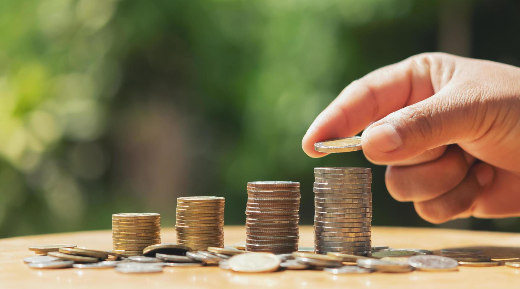 besparing geld hand- zetten munten Aan stack Aan tafel met zonneschijn. concept financiën en accounting foto