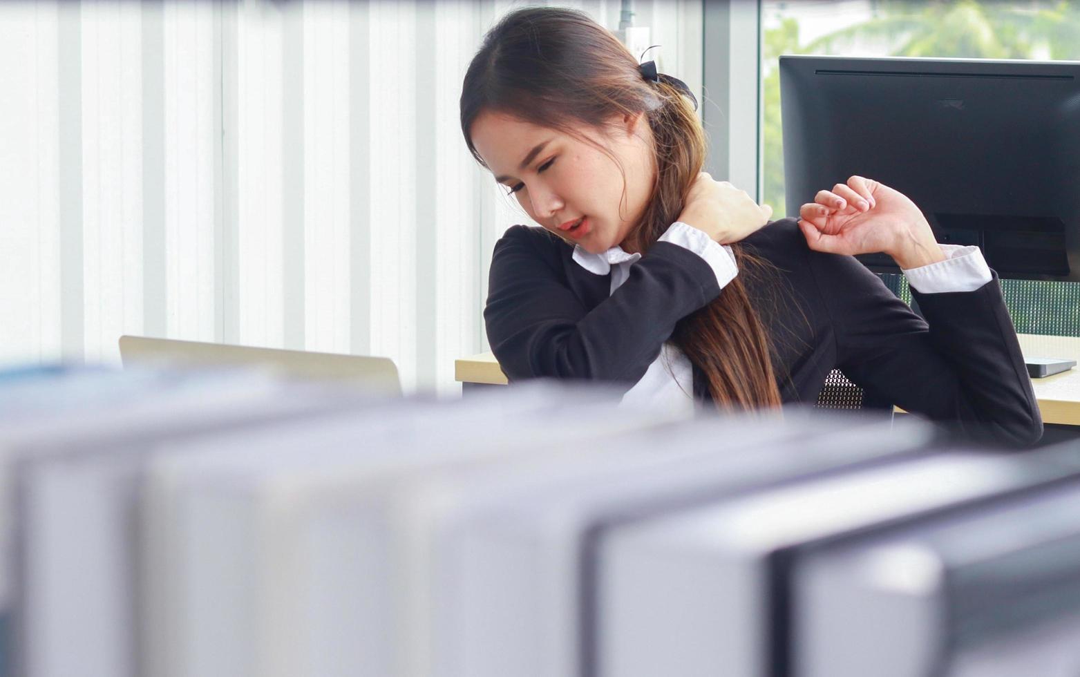 Aziatische vrouw op kantoor heeft pijn als gevolg van lange uren zitten foto