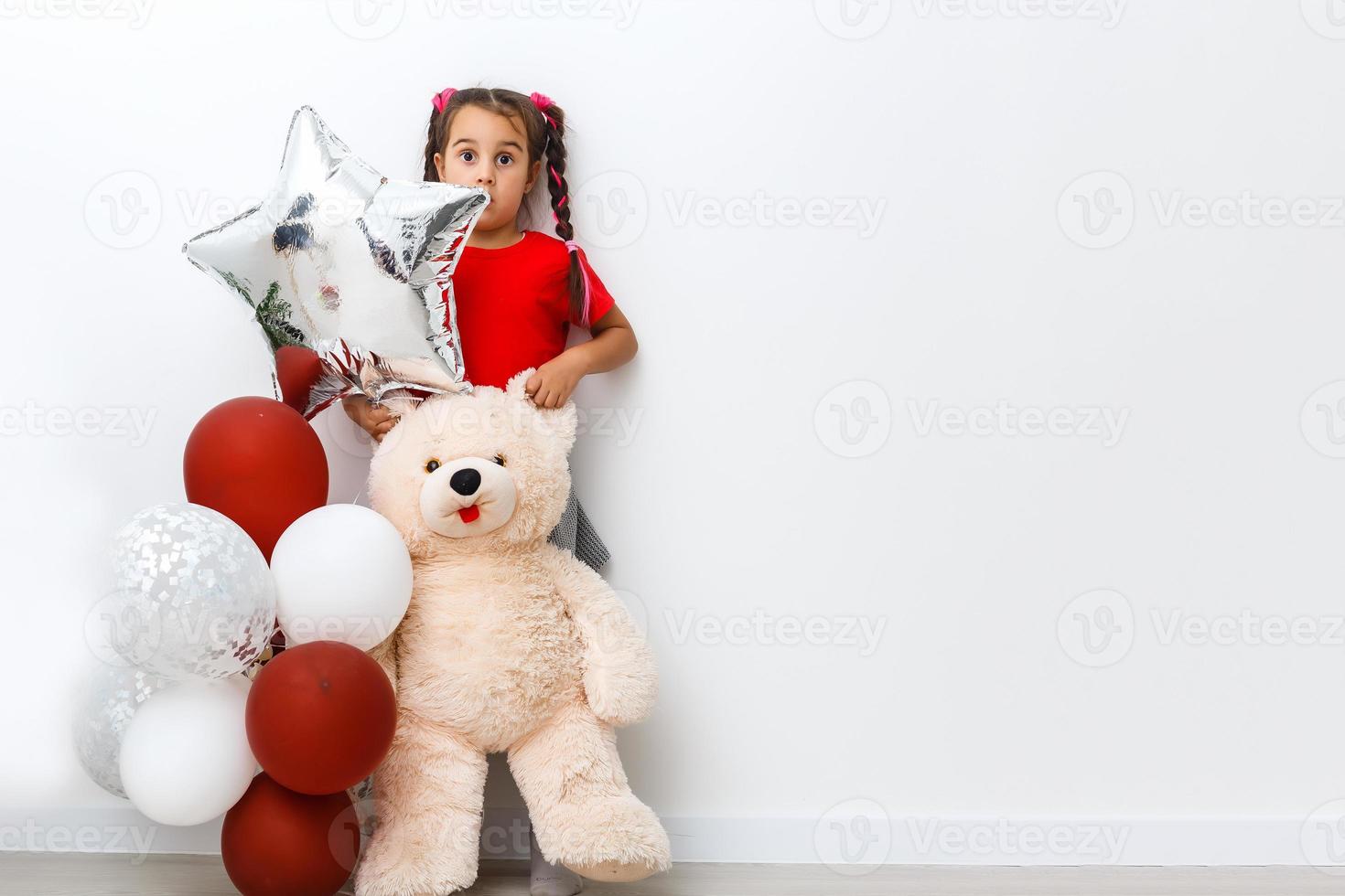 portret van glimlachen vrolijk meisje spelen met teddy beer in spel kamer. ze is fantaseren over lucht ballon foto