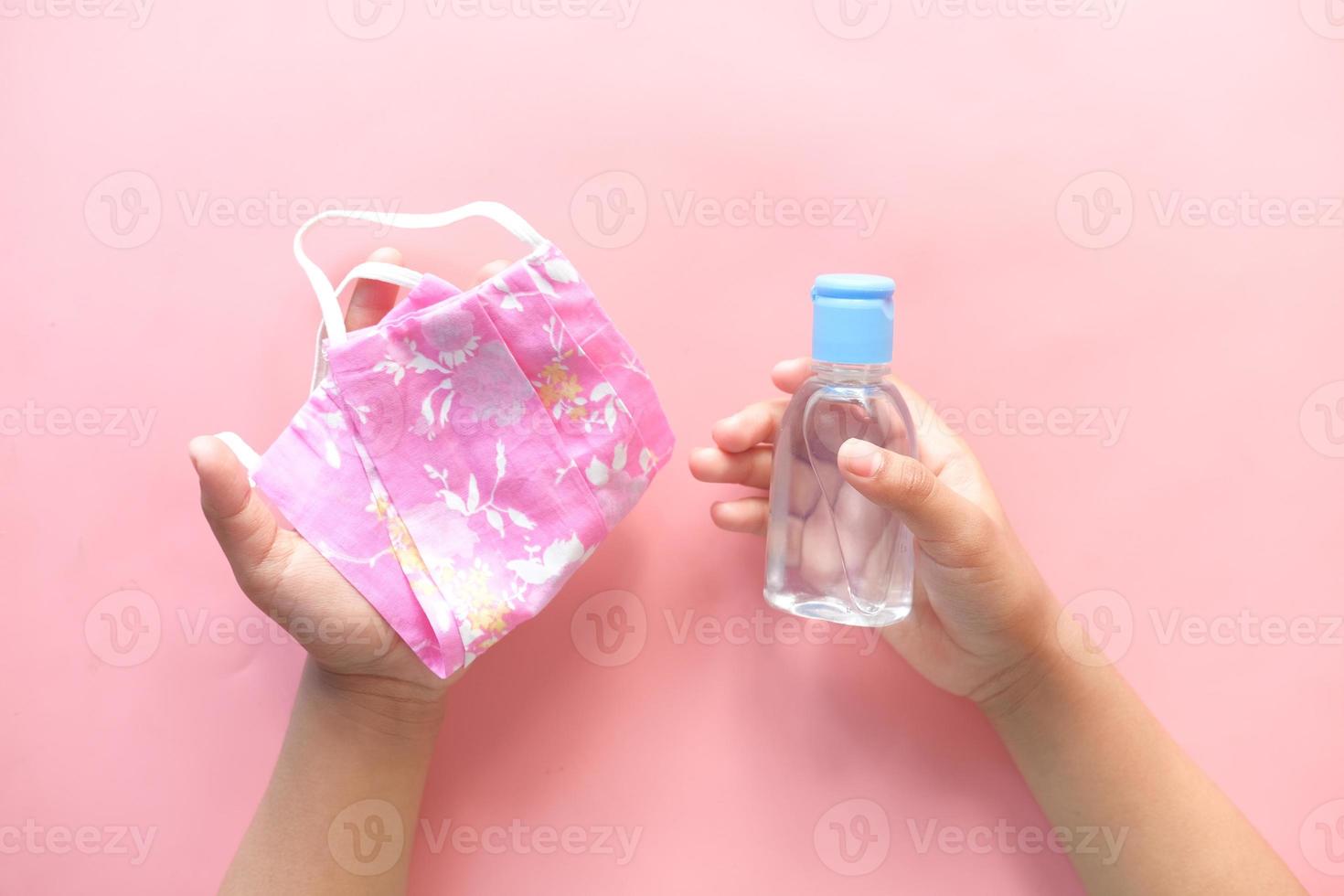 de handen van het kind met een roze masker en handdesinfecterend middel foto